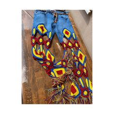 a pair of blue jeans with red and yellow designs on them sitting on top of a wooden floor