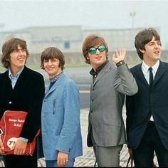 the beatles posing for a photo in front of an airport runway with their hand up