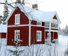 a red house with white trim and windows in the snow covered ground, surrounded by trees