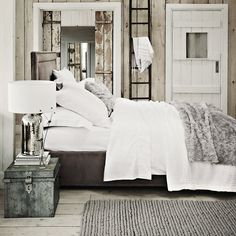 a bed with white linens and pillows in a rustic style bedroom, next to an antique trunk