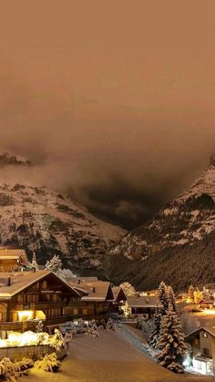 a snow covered mountain with houses in the foreground and lights shining on the mountains