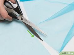 someone using scissors to cut fabric on a piece of blue paper with green arrow pointing at it