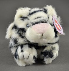 a black and white stuffed animal with pink nose sitting on a gray surface next to a tag