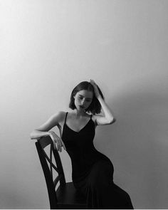 a woman sitting on top of a wooden chair wearing a black dress and holding her hair