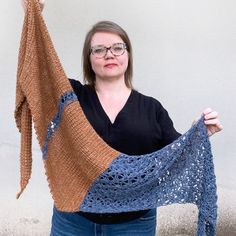 a woman holding up a blue and brown shawl with crochet on it