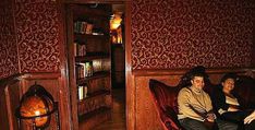 two people are sitting on a couch in a room with bookshelves and red wallpaper