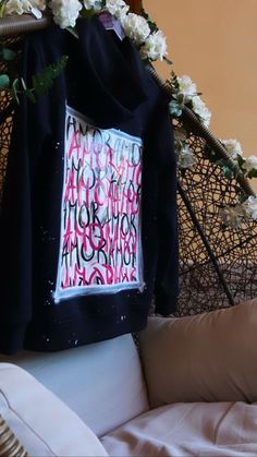 a black hoodie with pink and white letters on it sitting on a couch next to flowers