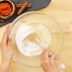 someone mixing ingredients in a bowl on top of a wooden table next to cinnamon sticks