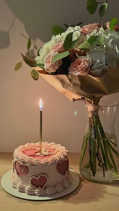 a birthday cake with a lit candle on it next to a vase filled with flowers