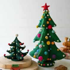 two felt christmas trees sitting next to each other on top of a wooden board with toys nearby