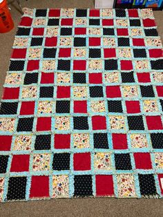 a red, black and white quilt is laying on the floor next to some books