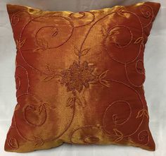 an orange pillow with gold thread work on it