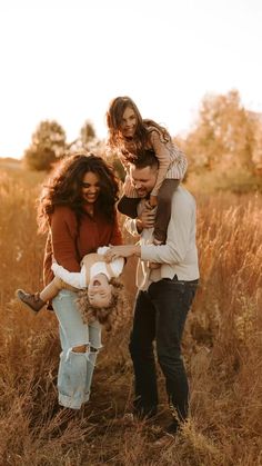 three people are standing in tall grass with one holding a baby and the other carrying an infant