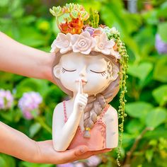 a statue of a girl with flowers on her head is being held by someone's hand