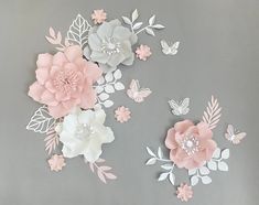 some pink and white paper flowers on a gray surface with butterflies flying around them,