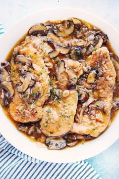 a white plate topped with chicken covered in mushrooms and gravy on top of a blue table cloth