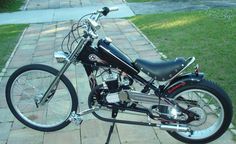 a black motorcycle parked on top of a brick walkway next to grass and trees in the background