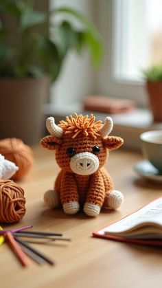 a small stuffed cow sitting on top of a wooden table next to yarn and crochet