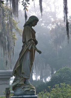 a statue in the middle of a park with moss hanging from it's ceiling