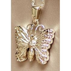 a silver butterfly pendant on a chain with a light brown fabric in the back ground