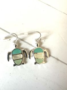 two small turtle shaped earrings with green and yellow colors on them, sitting next to each other