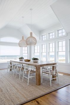 the dining room table is surrounded by white chairs and large windows with ocean view in the background