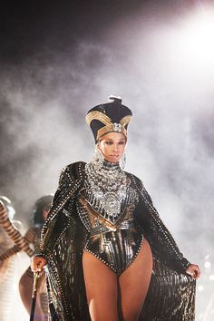 a woman in a black and gold outfit on stage with other people behind her wearing costumes