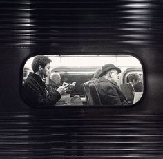 two men sitting on a train looking at their cell phones while another man looks out the window