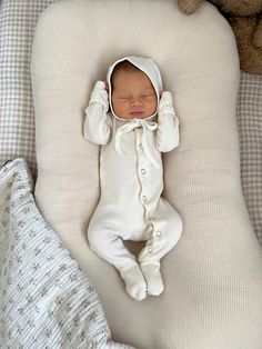 a baby in a white outfit laying on top of a pillow