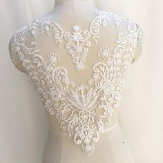 the back of a wedding dress with white lace on it and an open neckline