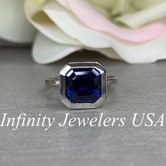 an image of a ring with a blue stone on it and flowers in the background