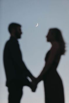 a man and woman holding hands with the moon in the background