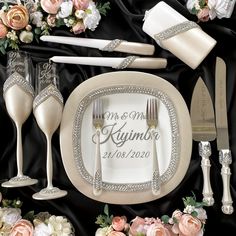 a table setting with champagne glasses, silverware and napkins on black satin background