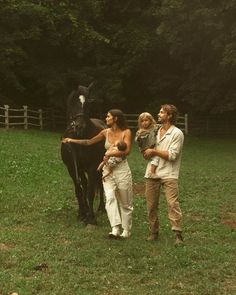 three people are walking with a horse in the grass near a fence and some trees