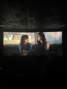 two women sitting in front of a large screen with their hands on their hipss