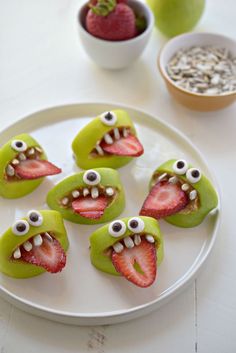 some green apples with faces and strawberries on them are sitting on a white plate