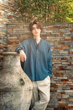 a young man standing next to a large vase in front of a brick wall and tree