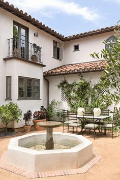 a fountain in front of a white building with tables and chairs around the outside area