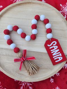 a red and white beaded necklace on a wooden plate with a tag that says santa