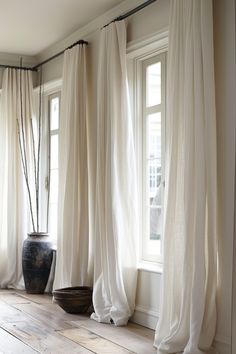 two vases sitting next to each other on top of a wooden floor in front of windows