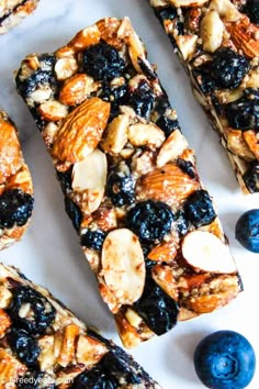 blueberry and almond granola bars on a white surface with fresh blueberries around them