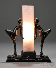 two statues are standing next to a light on a black stand with a white background