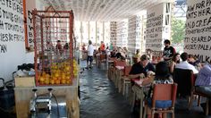 many people are sitting at tables with oranges in cages on the wall behind them