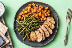 a plate with meat, green beans and sweet potatoes on it next to a fork