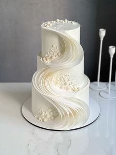 a three tiered cake with white icing on a table next to two candles