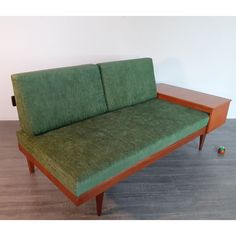 a green couch sitting on top of a hard wood floor next to a white wall