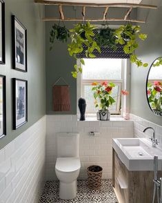 a white toilet sitting next to a bathroom sink under a window with potted plants