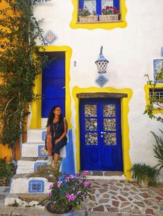 a woman standing in front of a blue and yellow building with flowers on the steps