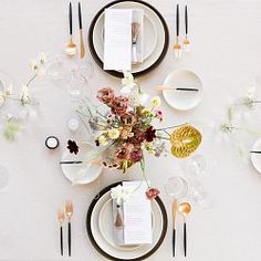 the table is set with white plates, silverware and floral centerpieces on it