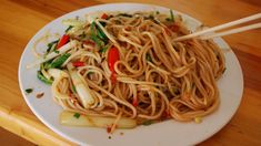 a white plate topped with noodles and veggies on top of a wooden table